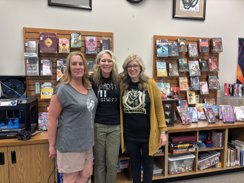 Three librarians stand in front of a slat wall and shelves displaying library books. 