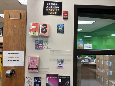 Books are displayed in acrylic book ledges as part of the Bengal Author Wall of Fame. A bookcase sits to the left of the display, and an office space is visible through a window on the right. 