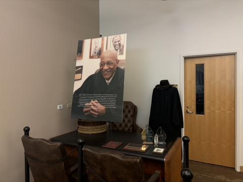 A photo of a Chicago judge sits on an easel next to several plaques and awards atop a wooden desk. 