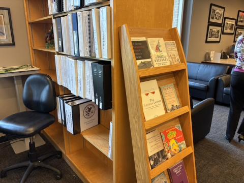 A wooden bookshelf holds binders of legal materials. At the end of a shelf, a vertical display rack adverstises various legal reading materials. 