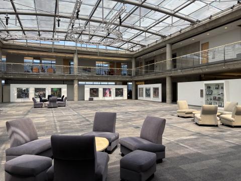 The library's two-story atrium features a glass roof and glass railings as well as several seating areas and artwork on the walls. 