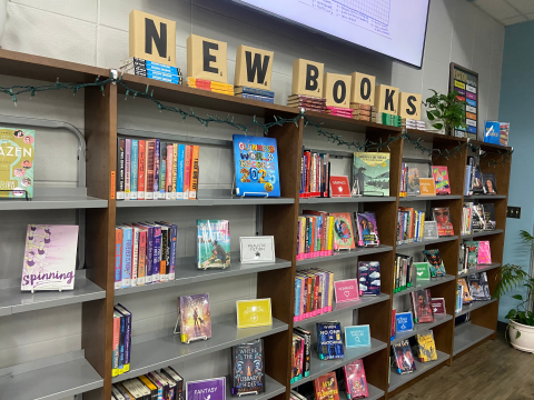 A library bookshelf along a wall is full of library books included in the new books display. 