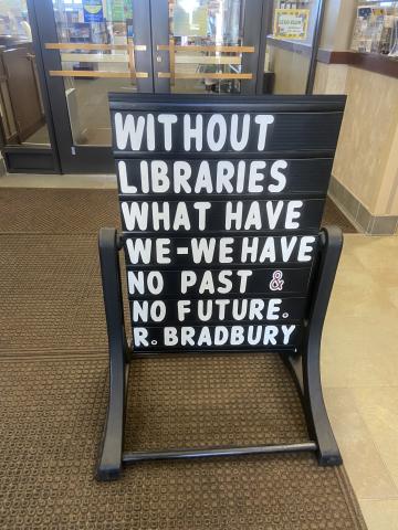 A black, reader board marquee sign stands in the entrance to the library and reads, "Without libraries what have we - we have no past & no future. --R. Bradbury" in white letters. 