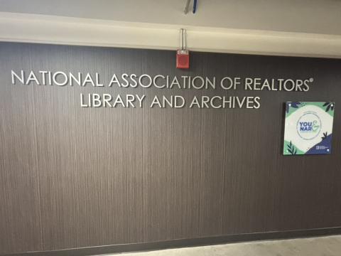 The sign for the National Association of Realtors Library and Archives comprised of white letteres on a walnut paneled wall. 